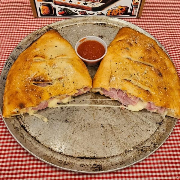 Two golden-brown calzones, split open to reveal ham and melted cheese, with a side of marinara.