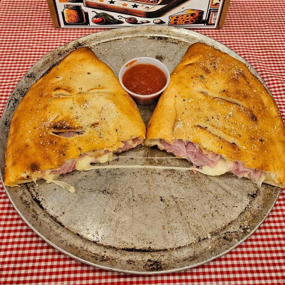 Two golden-brown calzones, split open to reveal ham and melted cheese, with a side of marinara.