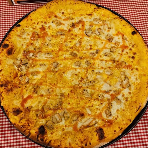 Tharptown General Store & Pizzeria's buffalo chicken pizza with cheese and sauce on a red and white checkered tablecloth.