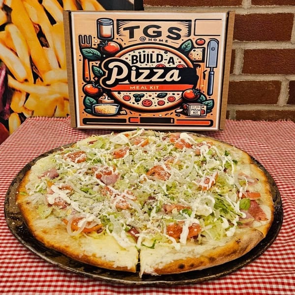A Tharptown General Store & Pizzeria "Build-A-Pizza" kit box behind a freshly made pizza.