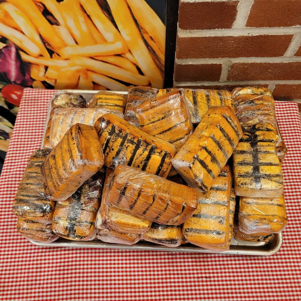 A tray of grilled cheese blocks wrapped in plastic, on a red and white checkered tablecloth.