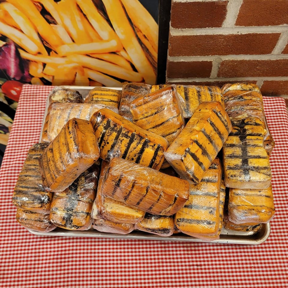 A tray of grilled cheese blocks wrapped in plastic, on a red and white checkered tablecloth.