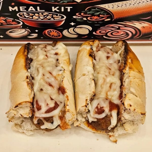 Two meatball subs with melted cheese and sauce on a white surface, with a "Meal Kit" graphic in the background.