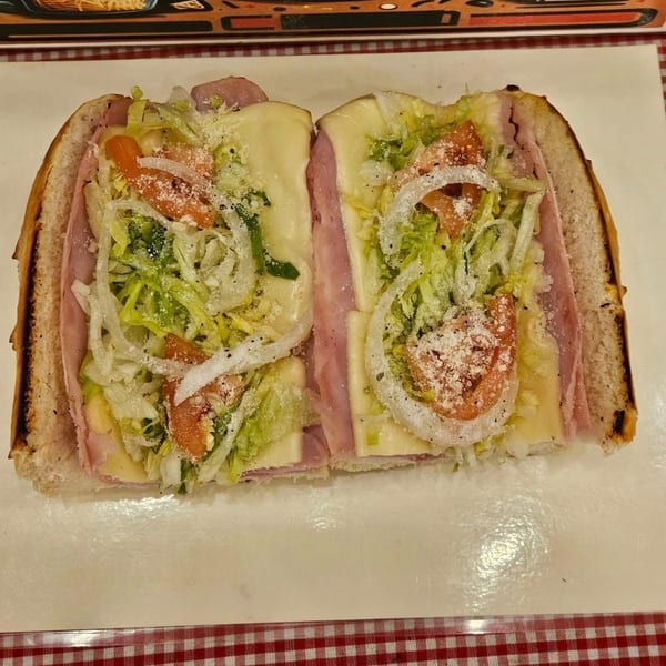 A large ham and cheese sub, cut in half, with lettuce, tomatoes, onions, and grated cheese.