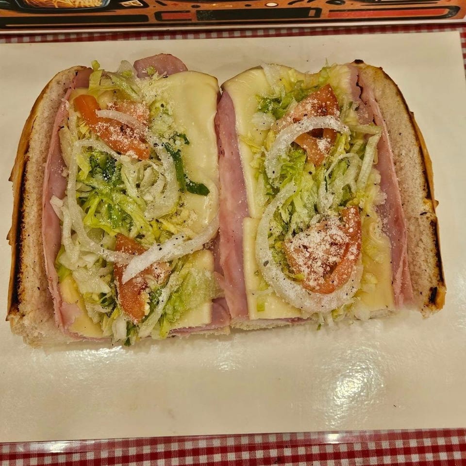 A large ham and cheese sub, cut in half, with lettuce, tomatoes, onions, and grated cheese.