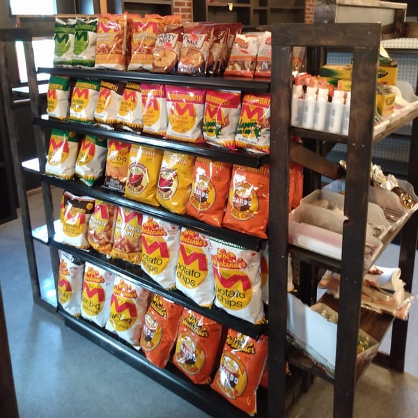 A wooden shelving unit filled with various bags of potato chips and snacks at Tharptown General Store.